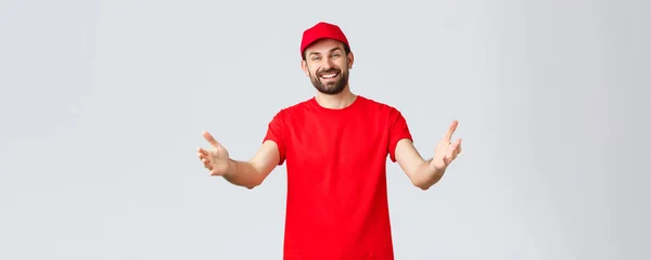 Compras online, entrega durante a quarentena e conceito takeaway. Correio agradável amigável na t-shirt e no tampão vermelhos, uniforme da empresa, alcançando mãos para o cliente ou a ordem, tomando o pacote — Fotografia de Stock