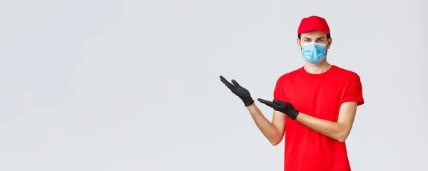 Groceries and packages delivery, covid-19, quarantine and shopping concept. Friendly delivery man in uniform, medical face mask and gloves introduce new promo, showing left banner — Stock Photo, Image