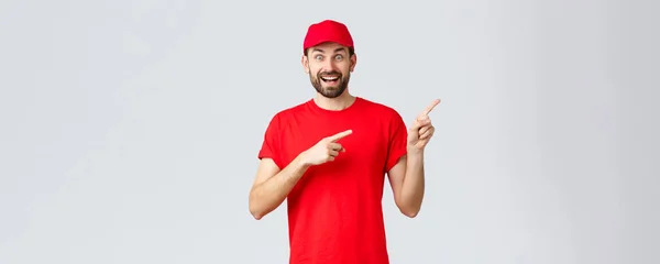 Shopping online, consegna durante la quarantena e il take away. Entusiasta sorridente corriere in uniforme rossa cap e t-shirt, indicando il dito destro, mostrando banner, consiglia offerta speciale — Foto Stock