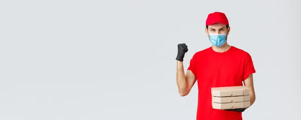 Food delivery, application, online grocery, contactless shopping and covid-19 concept. Fast and safe delivery, champions in industry. Courier in red uniform fist pump, deliver pizza order — Stock Photo, Image