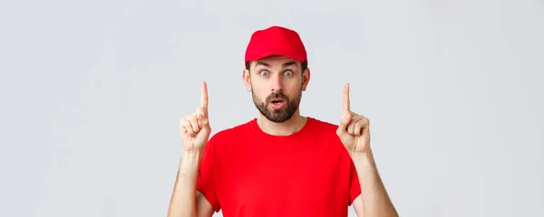 Online shopping, delivery during quarantine and takeaway concept. Surprised and impressed delivery guy, courier in red t-shirt and cap, pointing fingers up, gasping amazed, read interesting info — Stock Photo, Image