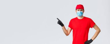 Covid-19, kendini karantina, online alışveriş ve nakliye konsepti. Sinirli teslimatçı kuryeyi azarlıyor. Transferde hata yapıyor, kaşlarını çatıyor, solu işaret ediyor. Tıbbi maske takıyor.