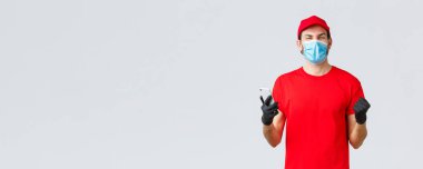 Bağlantı kurulamayan teslimat, ödeme ve kovid 19 sırasında online alışveriş, kendini karantina. Neşeli, kırmızı üniformalı mutlu kurye, eldivenler ve maske, gülümseme, uygulamada iyi haberler, cep telefonu