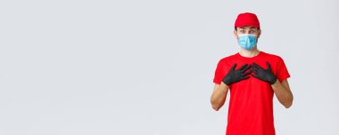 Covid-19, kendini karantina, online alışveriş ve nakliye konsepti. Benim için mi, dokunmuş ve şaşırmış teslimatçı çocuk hediye mi alıyor yoksa iltifat mı ediyor, göğsünü kabartıyor, yüz maskesi ve eldiven takıyor.