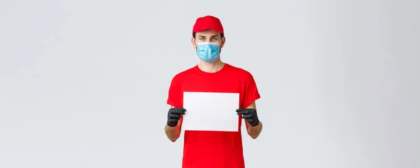 Covid-19, self-quarantine, online shopping and shipping concept. Express delivery guy during coronavirus tell stay safe home, buy internet, holding blank piece paper for your info, wear face mask — Stock Photo, Image