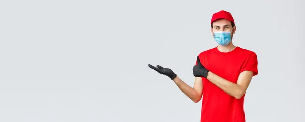 Groceries and packages delivery, covid-19, quarantine and shopping concept. Satisfied smiling courier in red uniform, face mask and gloves, holding promo banner in hand and thumb-up, recommend — Stock Photo, Image