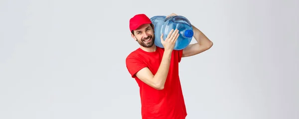 Takeaway, food and groceries delivery, covid-19 contactless orders concept. Friendly courier in red uniform bring bottled water on shoulder to your office or home, smiling cheerful — Stock Photo, Image