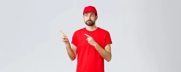 オンラインショッピング、隔離中の配達とテイクアウトの概念。赤のTシャツと帽子を着た従業員は失望した指を左上隅に向ける — ストック写真