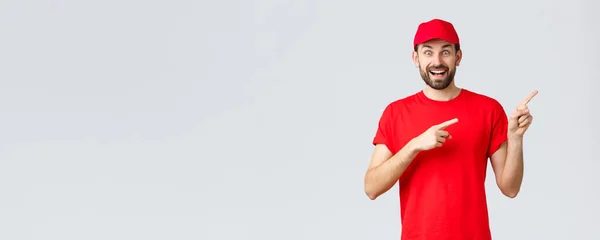 Compras online, entrega durante a quarentena e conceito takeaway. Entusiástico courier sorrindo em boné uniforme vermelho e t-shirt, apontando os dedos para a direita, mostrando banner, recomendo oferta especial — Fotografia de Stock