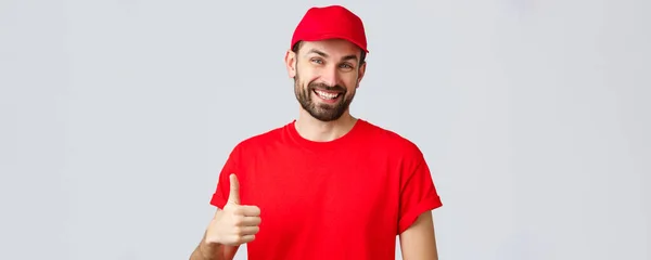 オンラインショッピング、隔離中の配達とテイクアウトの概念。フレンドリーで明るい赤いキャップとTシャツの制服を着た宅配便、インターネット注文、承認または推奨での親指アップを奨励します — ストック写真