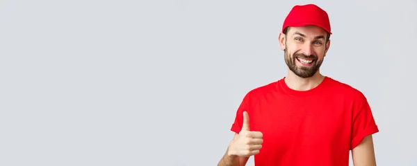 Compras en línea, entrega durante la cuarentena y concepto de comida para llevar. Mensajero amable y alegre en uniforme de gorra roja y camiseta, animar a hacer pedidos por Internet, pulgar hacia arriba en la aprobación o recomendación —  Fotos de Stock