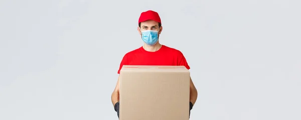 杂货和包裹递送，covid-19，检疫和购物概念。身穿红色制服、戴手套、戴防护面罩的信使，在验尸时将包裹箱送到病人家里 — 图库照片