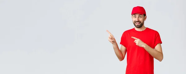 Nätshopping, leverans under karantän- och hämtningskoncept. Rolig och upphetsad leende kurir inbjudande klient ta en titt, anställd i röd uniform mössa och t-shirt pekar fingrarna vänster — Stockfoto