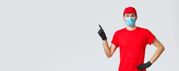 Covid-19, auto-quarantaine, achats en ligne et concept d'expédition. Livraison homme en casquette rouge et t-shirt, masque médical avec des gants pour protéger les clients et les employés, doigt pointant vers la gauche à la promo, montrer la publicité — Photo