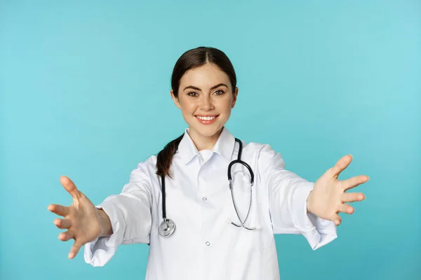 Smiling friendly doctor, girl healthcare worker, intern reaching hands, inviting, hugging or receiving in arms, standing over torquoise background — Stock Photo, Image