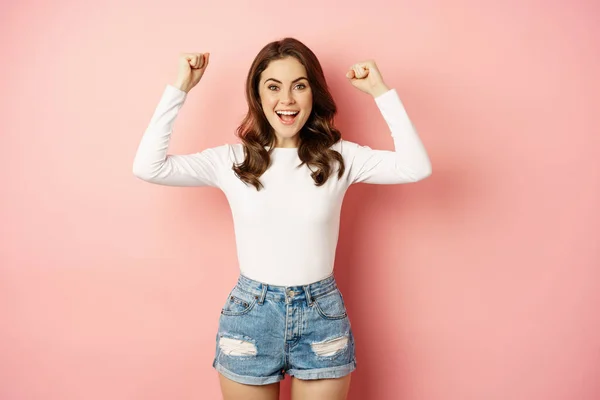 She is a winner. Enthusiastic brunette girl celebrating, jumping from happiness and shouting joyful, achieve goal success, standing over pink background — Foto de Stock