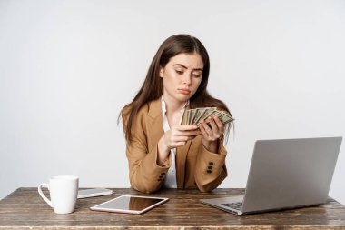 Sad businesswoman counting money in office with upset, disappointed face, low income, posing against white background