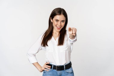 Confident young corporate woman pointing fingers at you camera, inviting, choosing, congratulating, standing over white background
