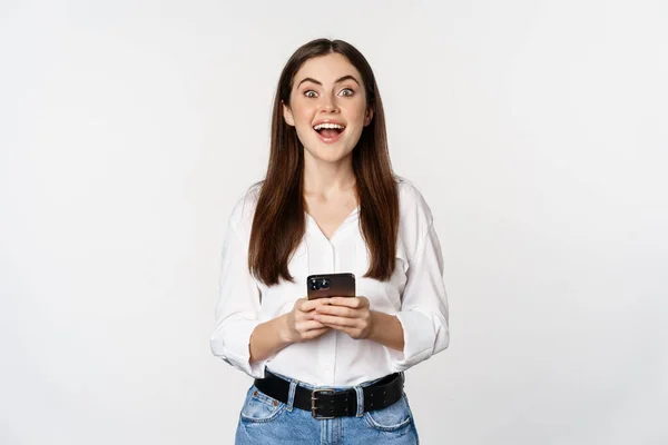 Young woman with smartphone, smiling and looking at camera, using mobile phone app, cellular technology and online shopping concept, white background — Foto Stock