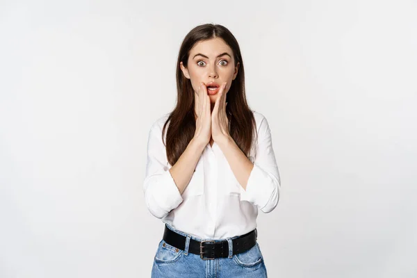 Surprised brunette woman looking amazed, seeing smth awesome, standing in blouse and jeans over white background — Stock fotografie