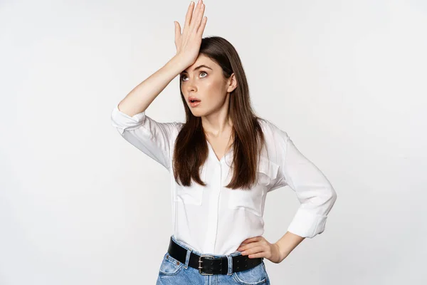 Annoyed young woman facepalm, slap forehead and roll eyes bothered, standing in white shirt and jeans over white background — Foto de Stock