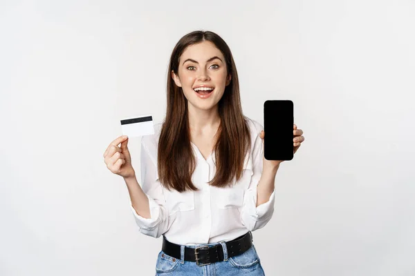 クレジットカードやスマートフォンの画面を表示する幸せな女性,オンラインショッピングの概念,アプリで購入,白い背景の上に立って — ストック写真