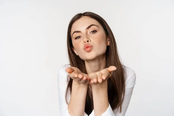 Feminine woman sending air kiss at camera, coquettish flirty pose, kissing, standing over white background — Zdjęcie stockowe