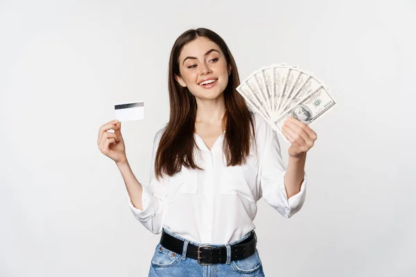 Happy modern woman holding money and credit card in hands, smiling pleased, standing over white background — Φωτογραφία Αρχείου