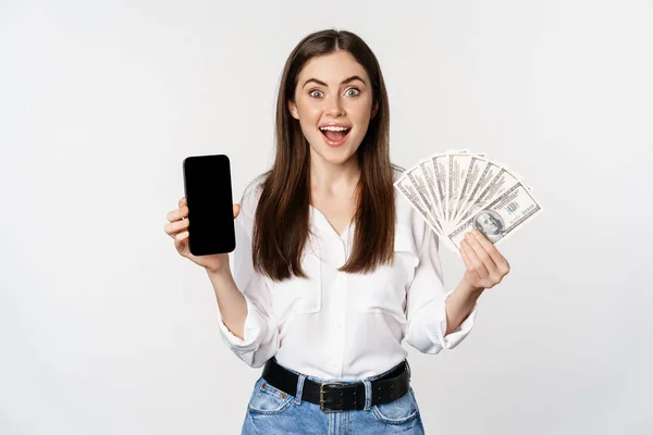 Woman showing mobile phone screen and cash, money, concept of microcredit and bank loans, standing over white background — Foto de Stock