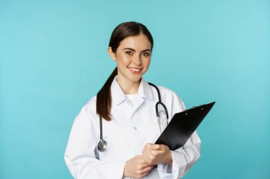 Image of professional woman doctor, physician with clipboard writing, listening patient at hospital clinic appointment, standing over torquoise background