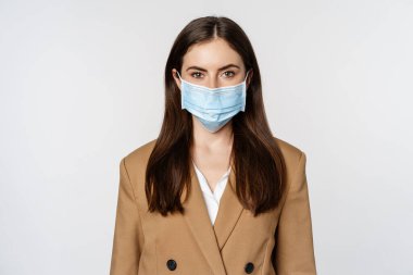 Workaplce and pandemic concept. Face portrait of businesswoman in medical mask and suit, looking serious at camera, going to work during covid-19