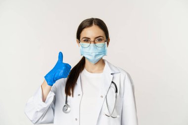 Coronavirus 'un yüz maskesi takmış kadın doktorların portresi. Baş parmaklarını gösterip gülümsüyor. Klinik ya da tıbbi web sitesi tavsiye ediyor.