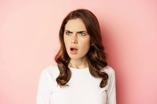 Close up portrait of confused, frustrated young woman, looking left with disappointment, puzzled by something, standing over pink background — Stock fotografie