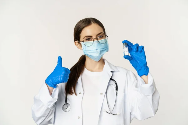 Närbild porträtt av ung professionell kvinnlig läkare, läkare i medicinsk ansiktsmask och glasögon, visar vaccin och godkänna det, rekommendera att vaccineras från covid-19 — Stockfoto