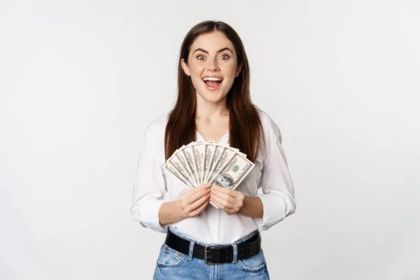 Porträtt av vacker kvinna som håller pengar, kontanter, leende nöjd, står över vit bakgrund — Stockfoto