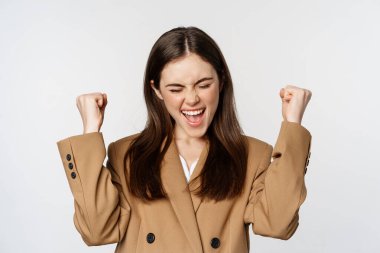 Enthusiastic girl screaming and rejoicing, looking at camera, winning, celebrating victory and triumphing, standing over white background