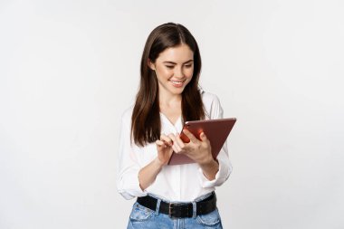 Portrait of smiling corporate woman looking at digital tablet, working, standing over white background