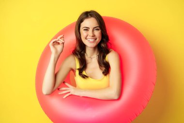 Güzel esmer kadın modelinin portresi pembe yüzme ringi, plaj aksesuarları ve yaz tatili konsepti, sarı arka plan.