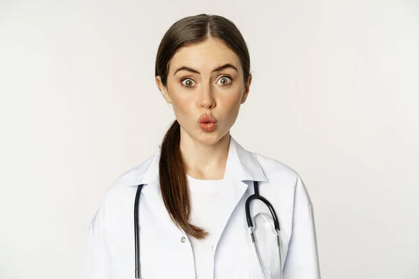 Portrait of woman doctor looking surprised, amazed, reaction of interest and amusement, standing in hospital uniform over white background — Zdjęcie stockowe