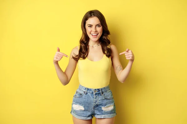 Happy attractive woman pointing fingers at herself, self-promoting, something personal, smiling and looking proud or confident, standing over yellow background — Fotografia de Stock