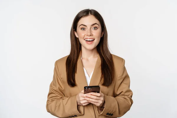 Smiling businesswoman using smartphone, app on mobile phone, standing over white background — Stockfoto