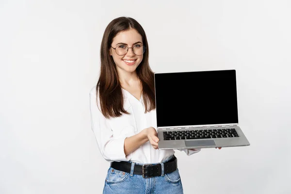 Портрет усміхненої жінки в окулярах, що показує екран ноутбука, демонструє веб-сайт компанії, промо-пропозицію, стоїть на білому тлі — стокове фото