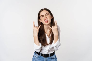 Rock n roll. Young woman showing rock on, heavy metal sign, having fun, standing carefree against white background