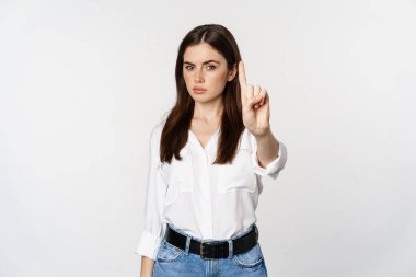 Serious woman showing taboo, stop gesture, shaking finger in disapproval, disagree, forbidding something, standing over white background