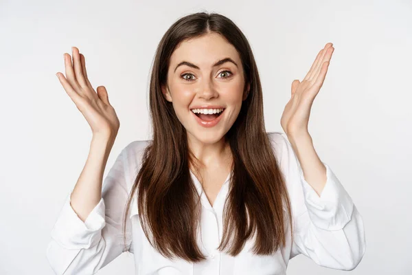 Enthusiastic young woman celebrating, smiling and raising hands up in rejoicing, winning and triumphing, standing over white background — Foto de Stock