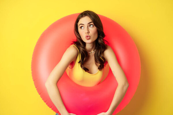 Close up portrait of coquettish young sexy woman inside pink swimming ring, concept of beach holiday, vacation and summer, yellow background