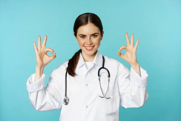 Smiling woman doctor, professional medical worker, showing okay, ok sign in approval, recommending clinic, quarantine campaign, torquoise background — ストック写真