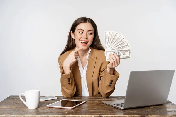 Portrait of businesswoman sitting in office with money, working and making profit income, posing happy against white studio background — Foto de Stock