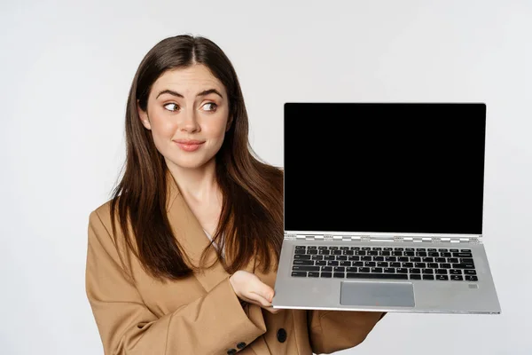 Молода жінка чіпляється і виглядає скептично, показуючи екран ноутбука, стоячи над білим тлом — стокове фото