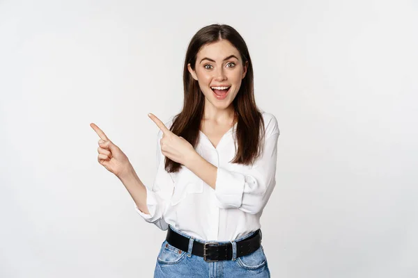 Portrait of enthusiastic smiling woman, female entrepreneur pointing fingers left and showing advertisement, showing announcement, white background — Fotografia de Stock